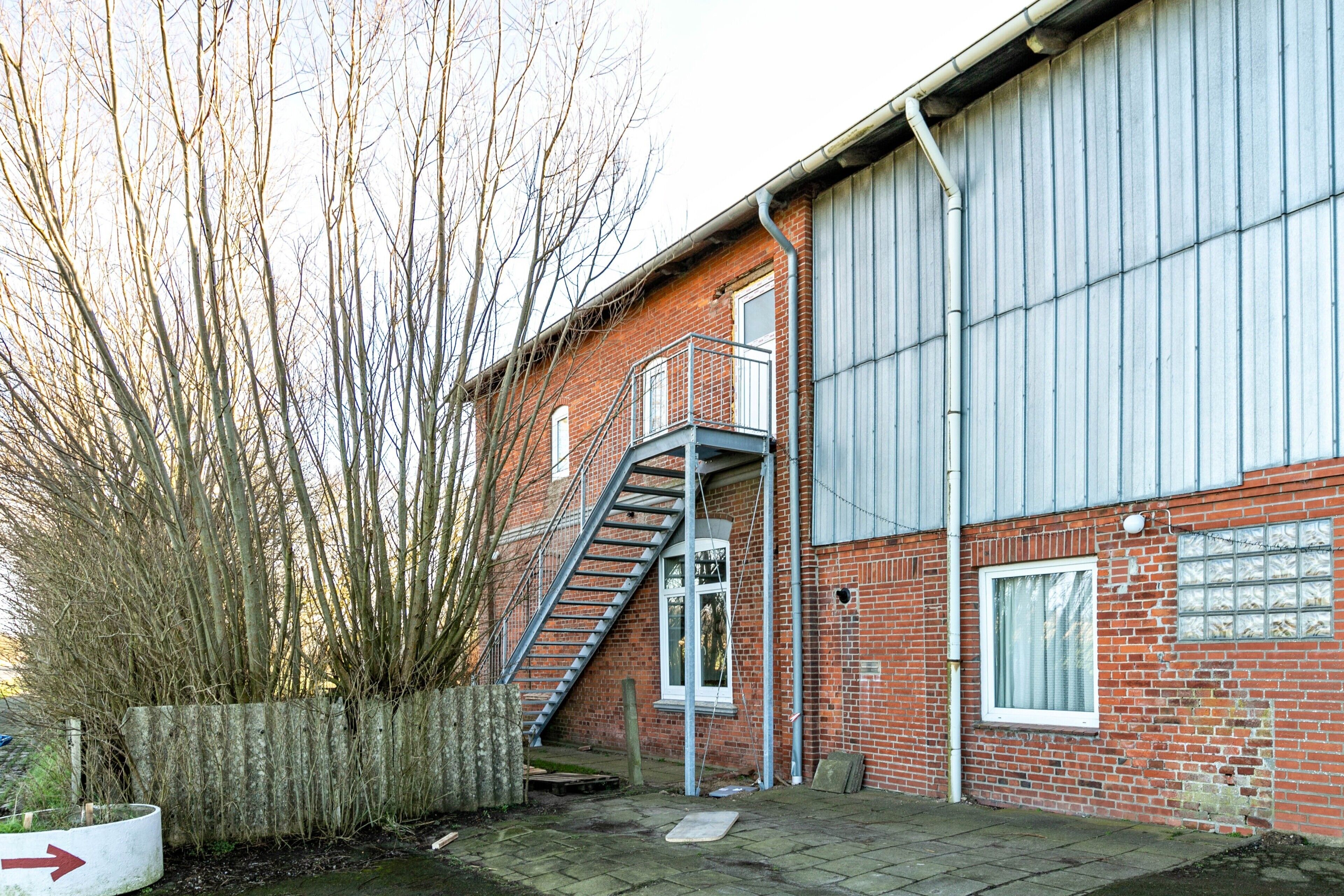 A brick building with a metal staircase leading to a window, a concrete wall, and a metal fence.