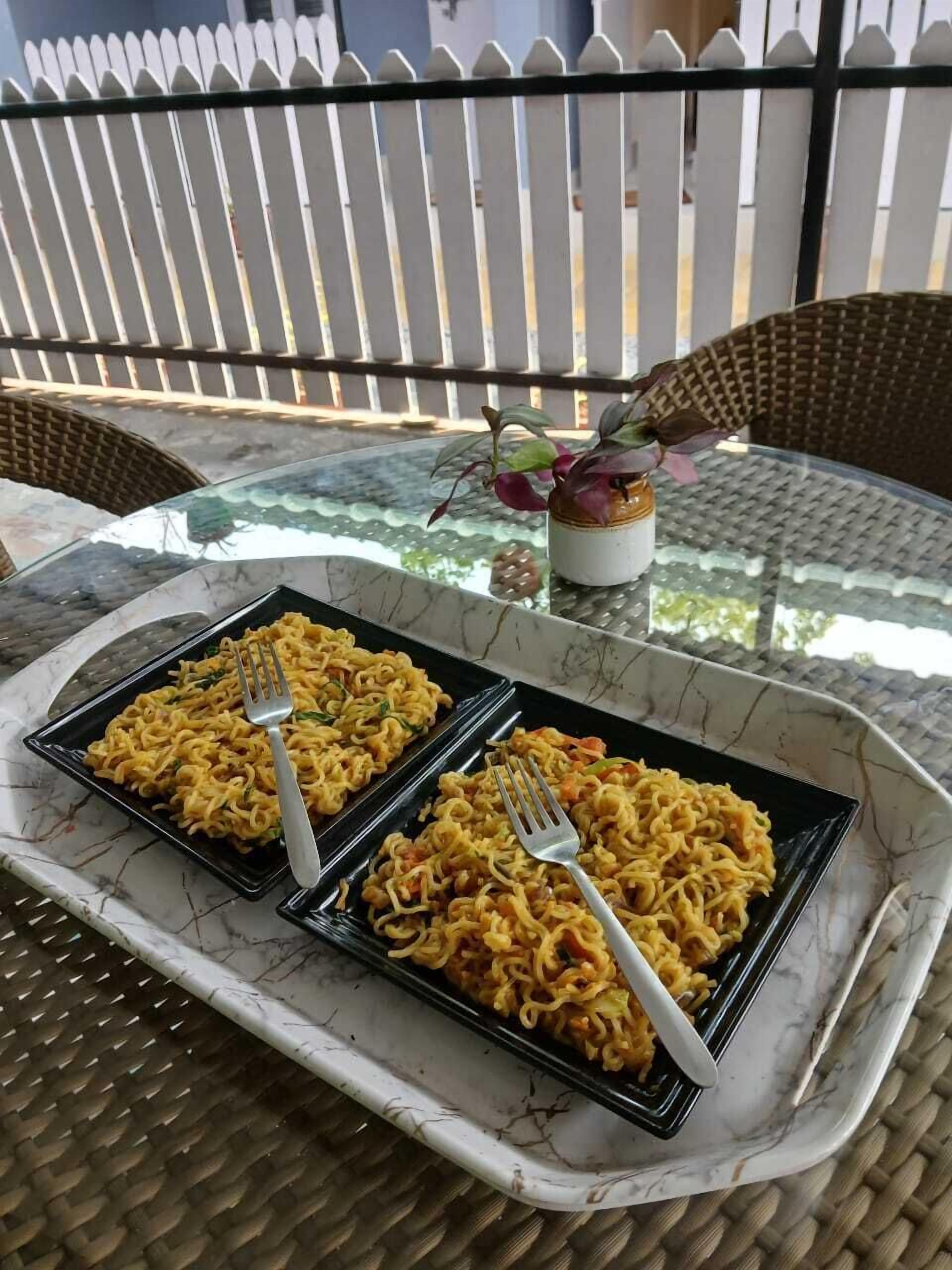 A dining table with two square plates of noodles, each with a fork.
