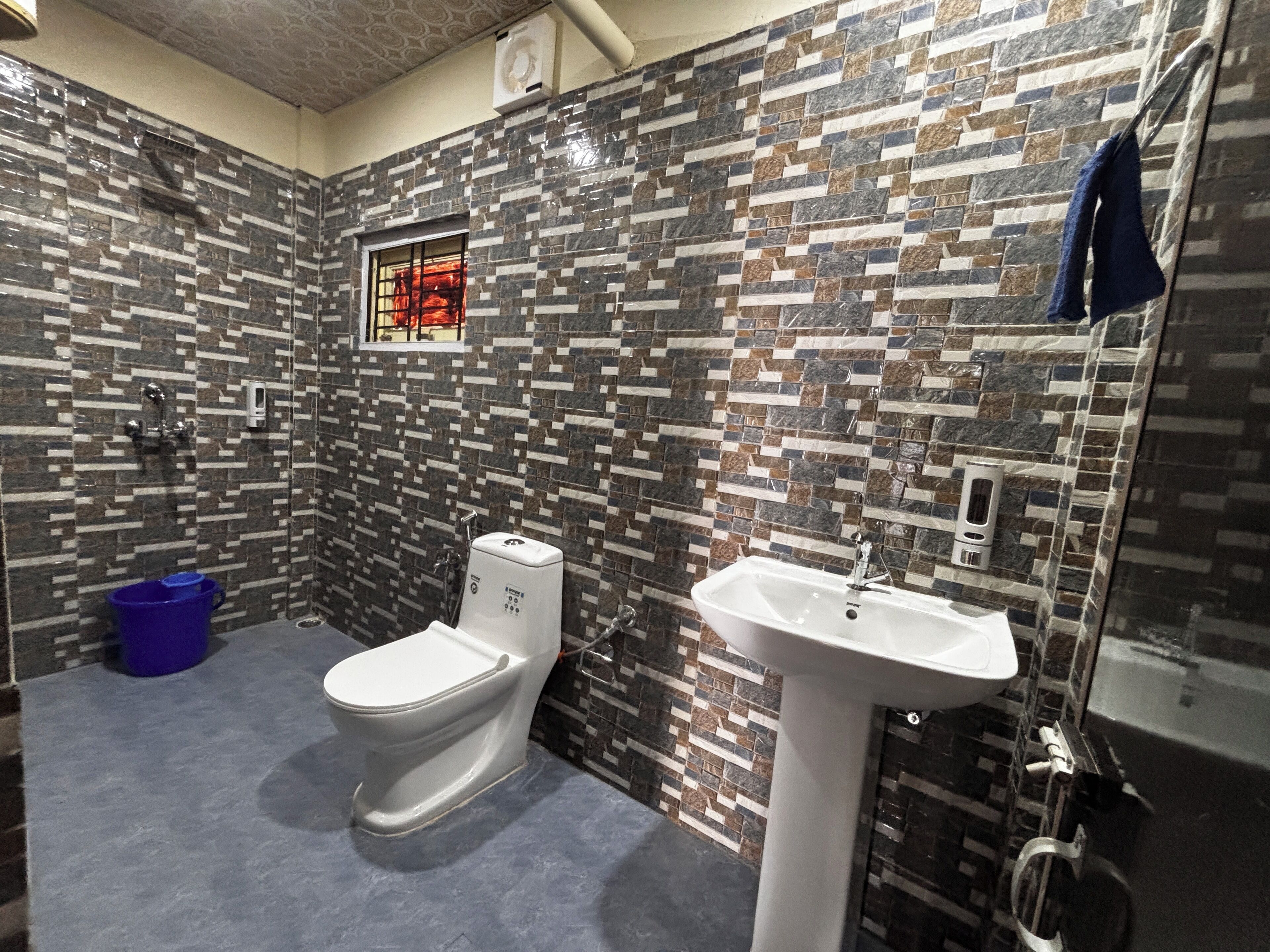 Ein Badezimmer mit Toilette, Waschbecken und Dusche. Die Wände sind mit einem Mosaikmuster gefliest.