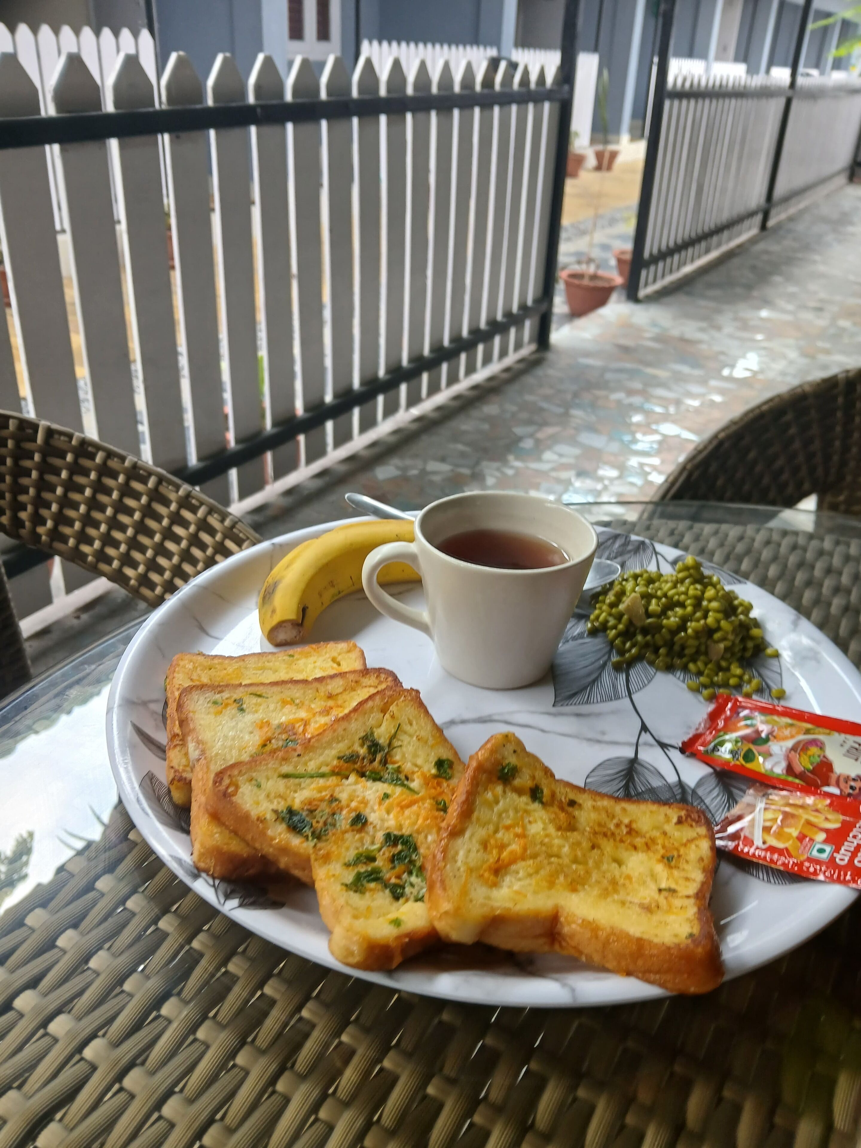 Una mesa con una tostada, un plátano, una taza de té y guisantes verdes.