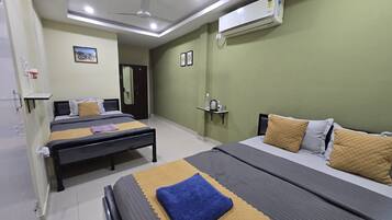 Habitación de hotel con dos camas, ventilador de techo, unidad de aire acondicionado, mesita de noche, espejo y estante pequeño con artículos de tocador.