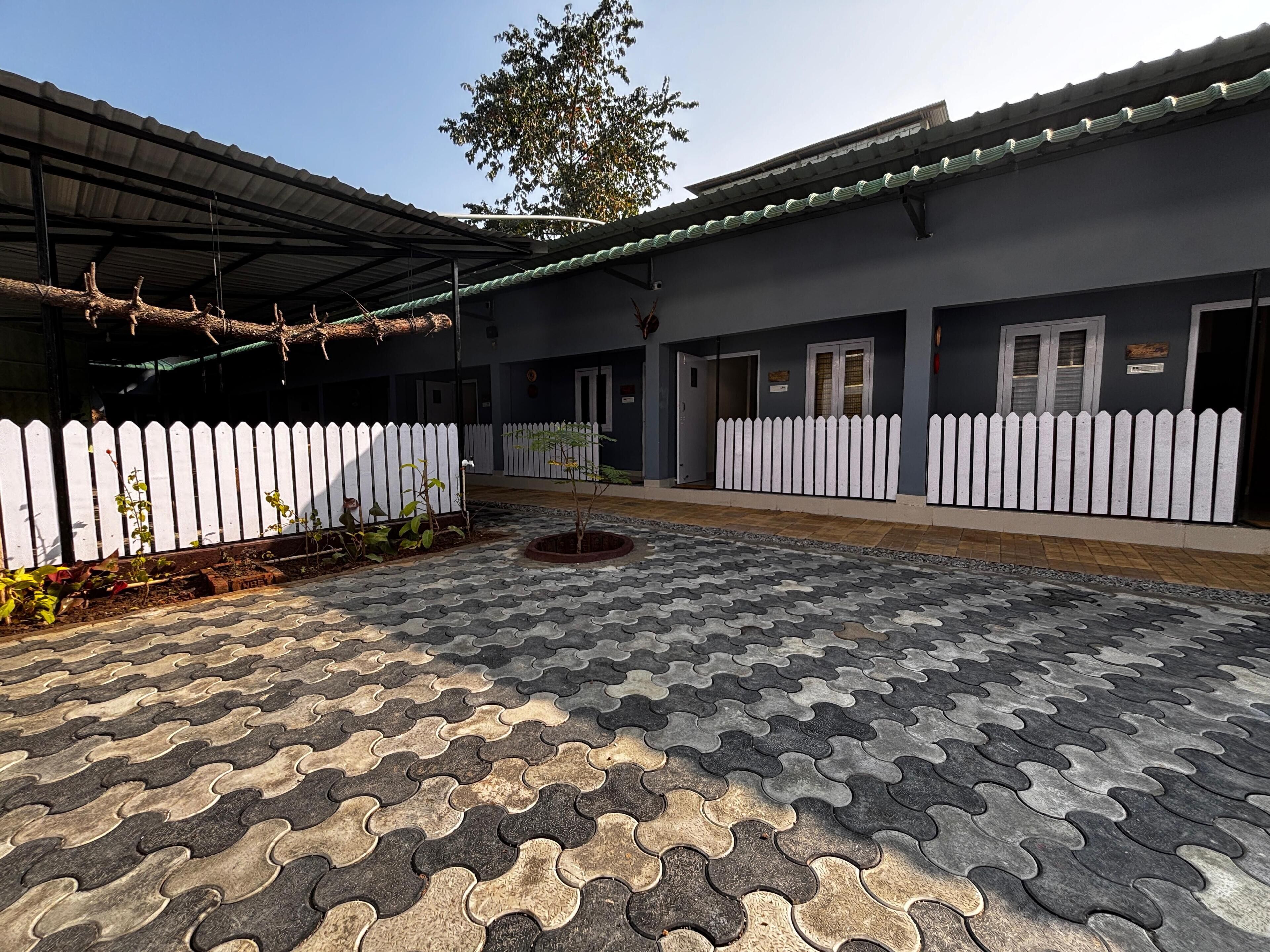 A courtyard with interlocking paving tiles, a white picket fence, and a building with a dark facade and a green roof.