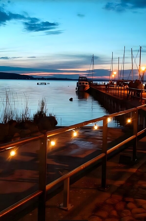 A pier with a boat docked, a walkway with string lights, and a calm body of water.