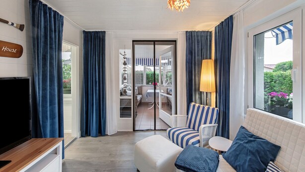 A room with a TV, a sofa, a lamp, and a view of an outdoor seating area.
