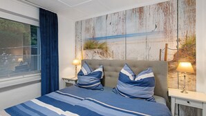 A bedroom with a bed, two nightstands, a window with curtains, and a wall with a beach-themed artwork.
