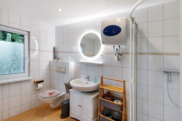 Baño con inodoro, lavamanos, espejo y ducha.