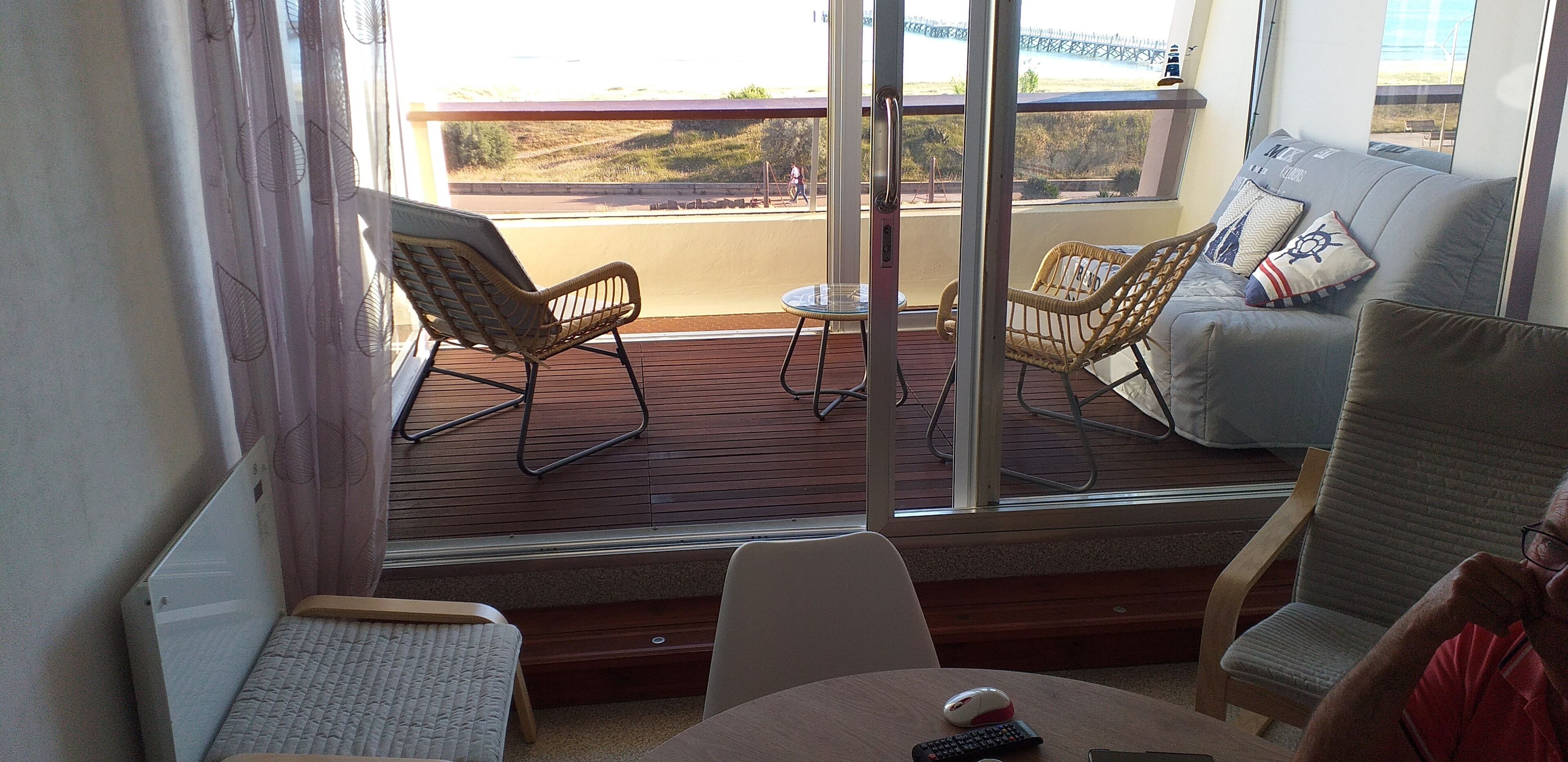 Een balkon met rieten stoelen, een kleine tafel en een bank met kussens in nautische stijl.