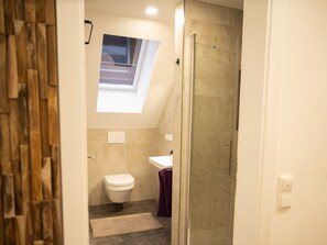 Een badkamer met dakraam, toilet, wastafel en douche.