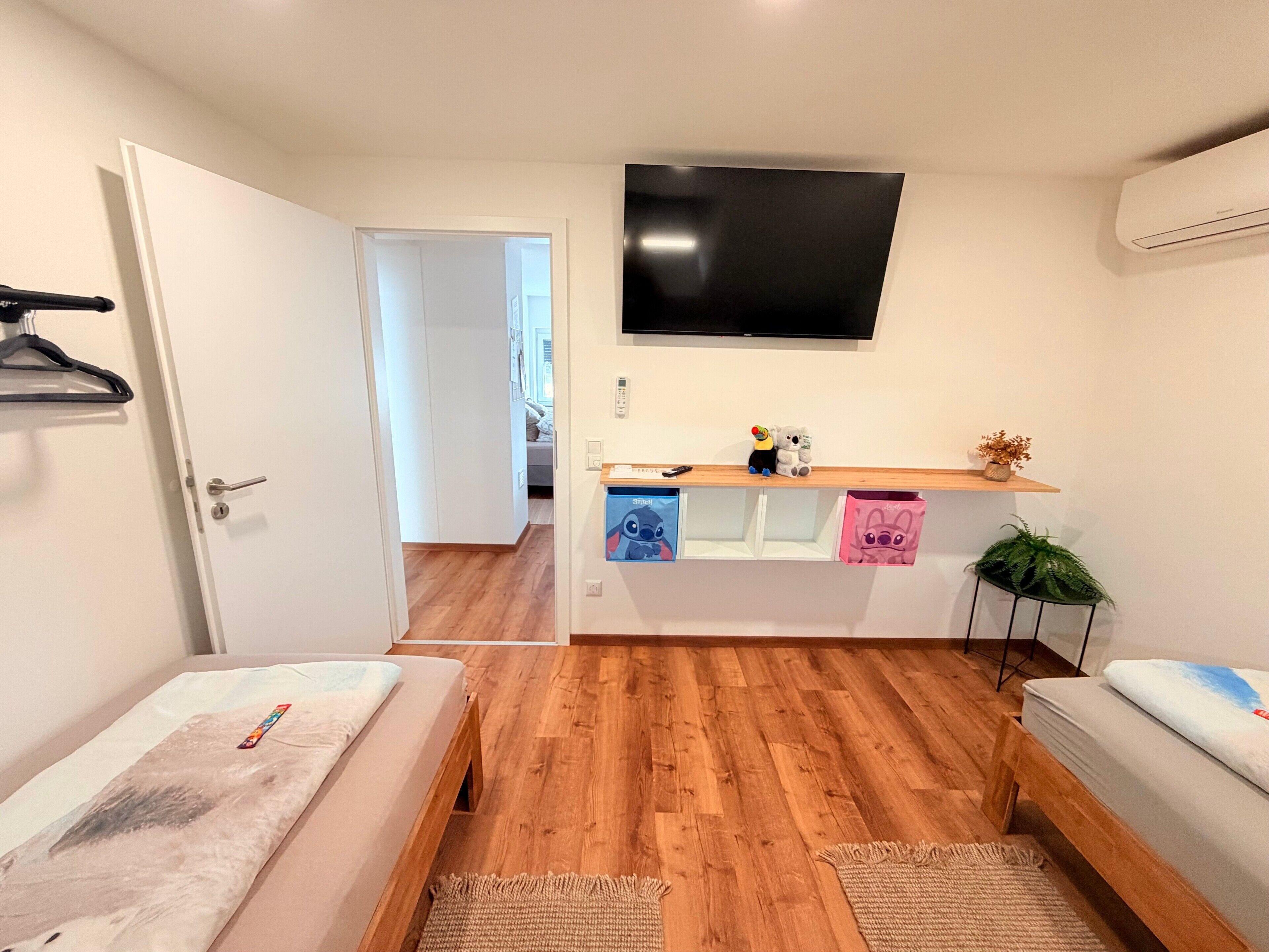 A bedroom with a bed, a TV, a shelf with toys, and a door leading to another room.