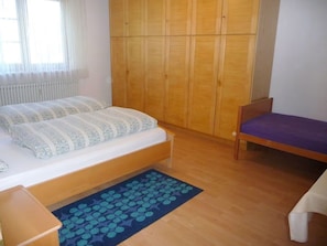 A bedroom with a bed, a chair, a wardrobe, and a window.