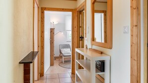 Un pasillo con paredes de madera, una consola blanca, un espejo y una silla con cojín a rayas.