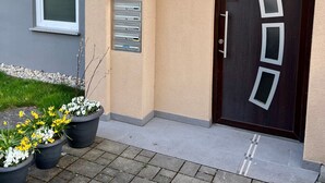Una entrada moderna de edificio con una puerta marrón oscuro, un buzón y plantas en macetas.