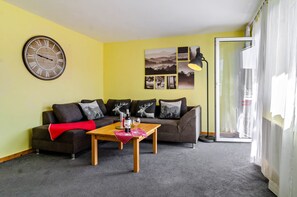 A living room with a sofa, a coffee table, a clock, and a window with curtains.