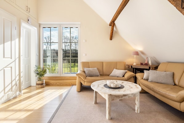 A modern living room with a beige sofa, a round coffee table, and a large window with a view of trees.