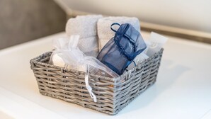 Een rieten mand met een witte handdoek, een blauwe netzak en een witte plastic tas op een witte ondergrond.