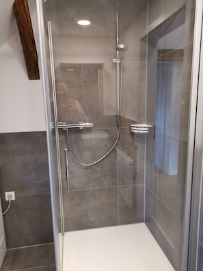 A modern shower enclosure with a glass door, a handheld showerhead, and a wall-mounted faucet.