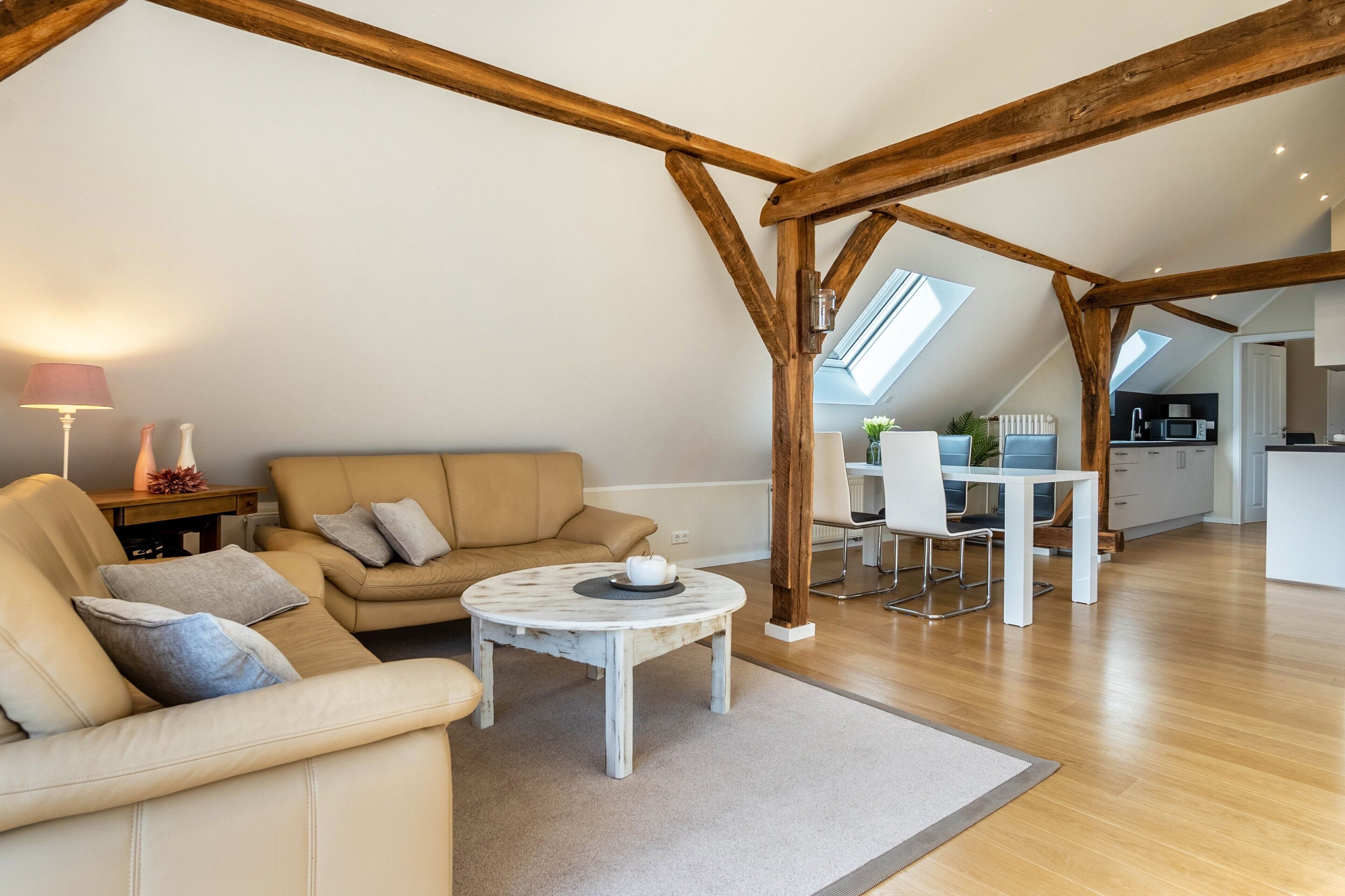 Ein geräumiger Loft mit hohen Decken, freiliegenden Holzbalken, einem runden Couchtisch, einer Couch und einem Essbereich mit einem weißen Tisch und Stühlen.