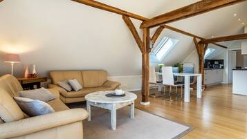 Ein geräumiger Loft mit hohen Decken, freiliegenden Holzbalken, einem runden Couchtisch, einer Couch und einem Essbereich mit einem weißen Tisch und Stühlen.