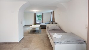 Ein Zimmer mit einem Bett, einer Couch, einem kleinen Tisch und einem Fenster mit Vorhängen.