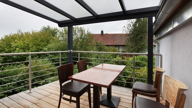 Ein Balkon mit Tisch und Stühlen, einem Metallgeländer und Blick auf Grünflächen sowie ein Gebäude im Hintergrund.