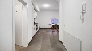 A narrow hallway with a kitchen area, a dining table with chairs, and a white telephone on the wall.