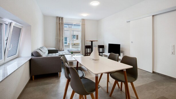 A modern living room with a sofa, dining table, chairs, and a TV.
