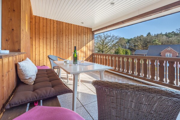 Un balcon en bois avec une table, des chaises et un fauteuil en osier.