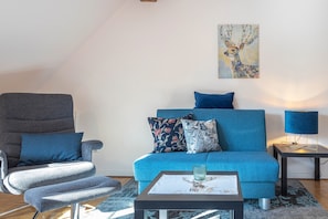 Un salon avec un canapé bleu, un fauteuil gris et une petite table sur laquelle se trouve un verre.
