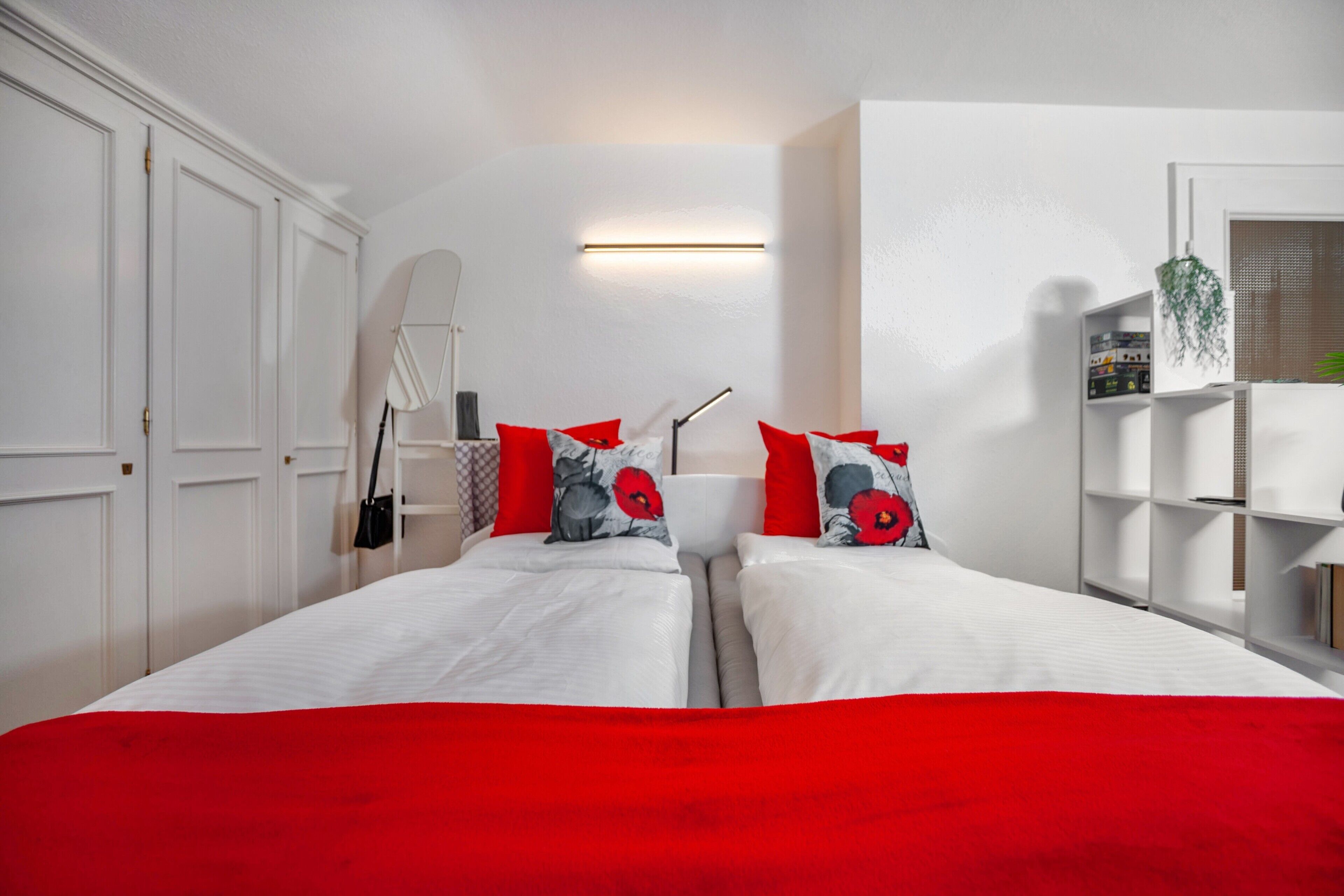 Ein Schlafzimmer mit zwei Betten, weißen Wänden, einer roten Bettdecke und einer weißen Decke.
