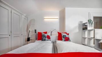 Ein Schlafzimmer mit zwei Betten, weißen Wänden, einer roten Bettdecke und einer weißen Decke.
