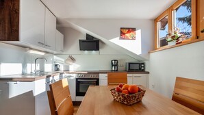 A modern kitchen with white cabinets, a wooden dining table, and a fruit basket.