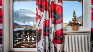 A room with a view of snow-covered mountains, a window with red curtains, a radiator, and a potted plant on the windowsill.