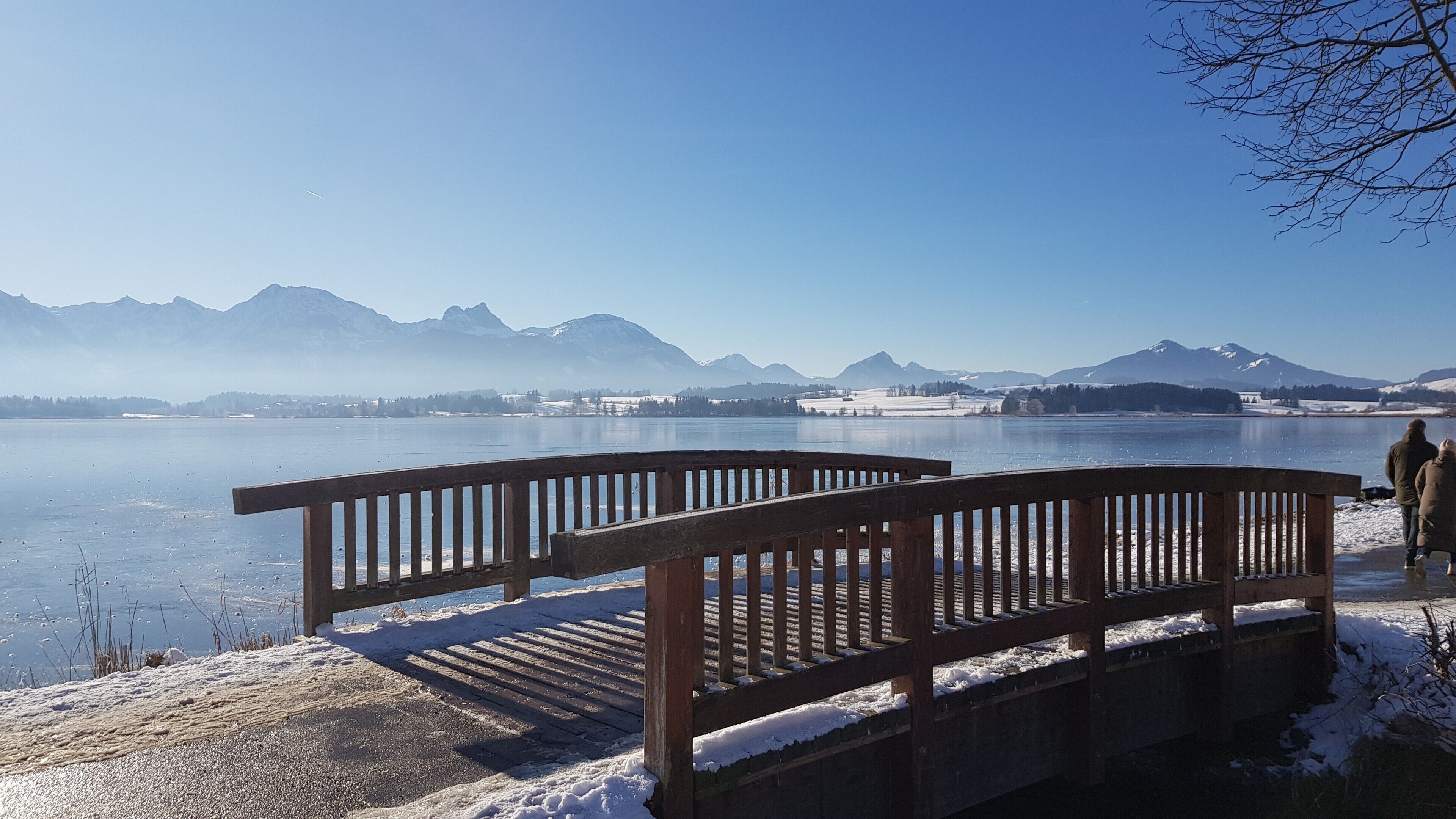 A bench by a frozen lake with mountains in the background.
