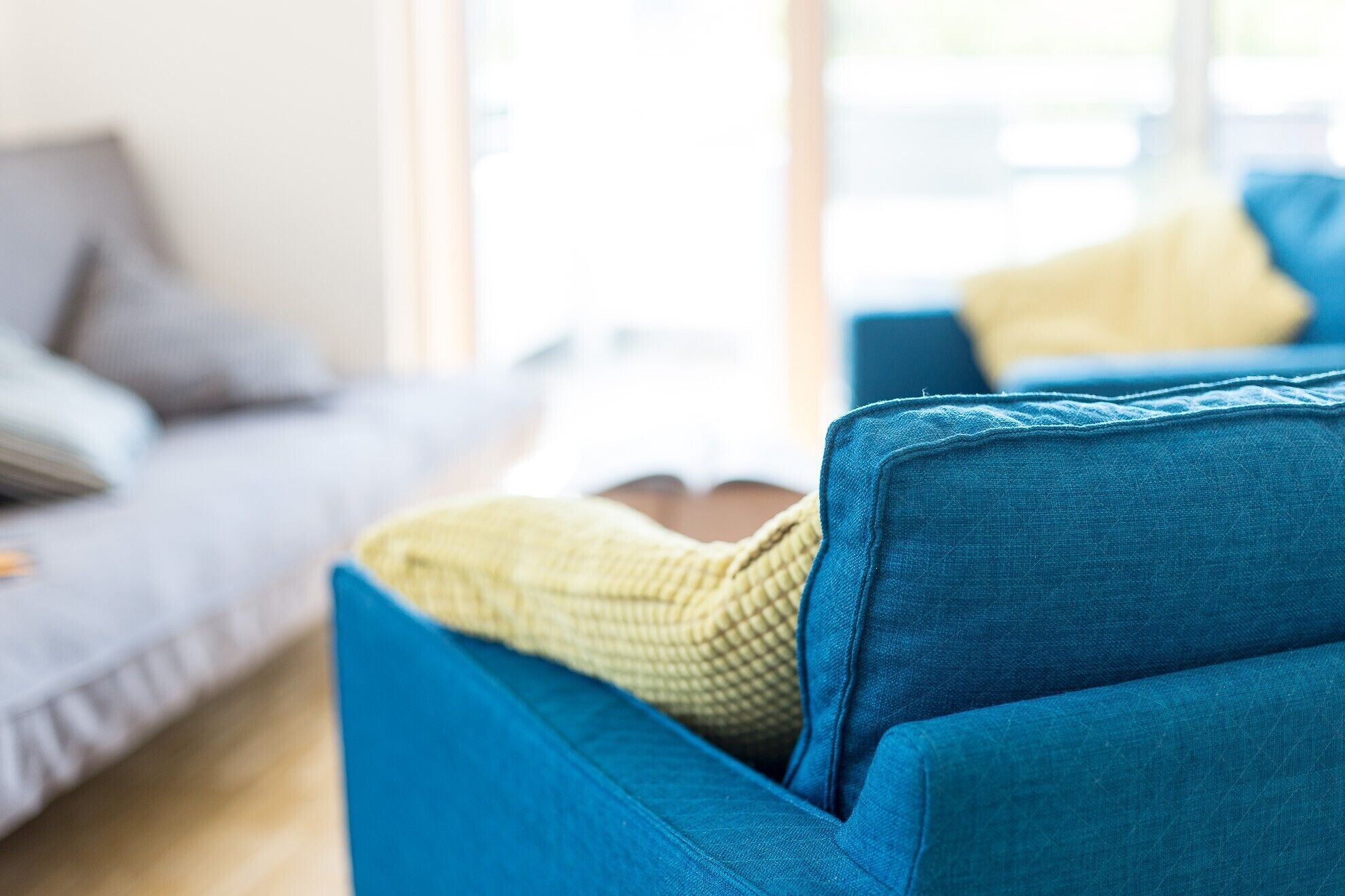 Ein blaues Sofa mit einer gelben Decke und ein graues Sofa im Hintergrund.