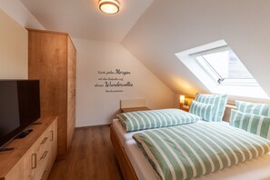 A bedroom with a wooden wardrobe, a bed with striped bedding, a television on a wooden cabinet, and a skylight. - Apartment 'Vogelsberg' with Shared Terrace, Shared Garden and Wi-Fi (Wächtersbach)