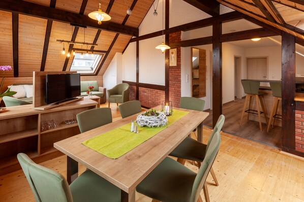 A dining area with a wooden table, green chairs, and a TV in the background. - Apartment 'Spessart' with Shared Terrace, Shared Garden and Wi-Fi (Wächtersbach)
