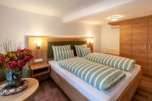 A modern bedroom with a bed, bedside tables, a wooden wardrobe, and a vase of flowers. - Apartment 'Spessart' with Shared Terrace, Shared Garden and Wi-Fi (Wächtersbach)