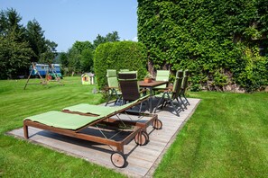 A wooden deck with lounge chairs and a table, surrounded by a well-maintained lawn and a large hedge. - Apartment 'Spessart' with Shared Terrace, Shared Garden and Wi-Fi (Wächtersbach)
