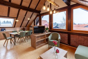A modern interior with a dining area, a TV, and a view through large windows. - Apartment 'Spessart' with Shared Terrace, Shared Garden and Wi-Fi (Wächtersbach)