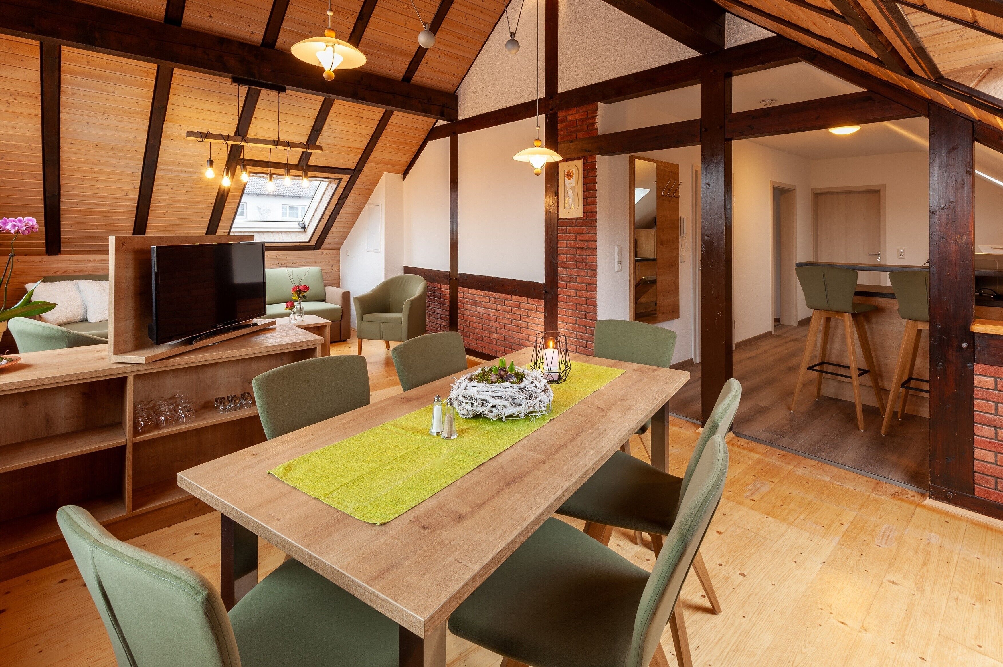 A dining area with a wooden table, green chairs, and a TV in the background.