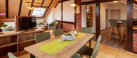 A dining area with a wooden table, green chairs, and a TV in the background.