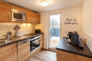A modern kitchen with wooden cabinets, a built-in microwave, a coffee maker, and a glass on the counter.