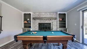 Une table de billard avec des billes, une cheminée en briques et des étagères dans une pièce au plancher en bois.