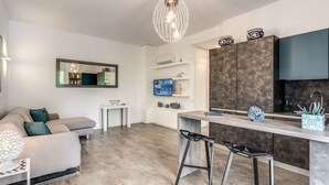 Une cuisine moderne avec un revêtement mural foncé, des meubles blancs et un four encastré. On y trouve également un coin bar avec des tabourets et une petite table.