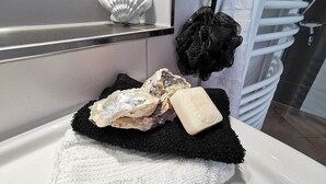Um banheiro com uma banheira branca, tapete de banho preto, toalha branca e uma concha decorativa na parede.