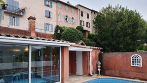A swimming pool with a glass enclosure, a covered patio, and a red brick wall. - Village House in France with Private Pool (Bagnols-en-Forêt)