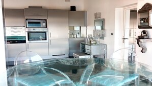 A modern kitchen with built-in appliances, a glass dining table, and decorative items. - Village House in France with Private Pool (Bagnols-en-Forêt)