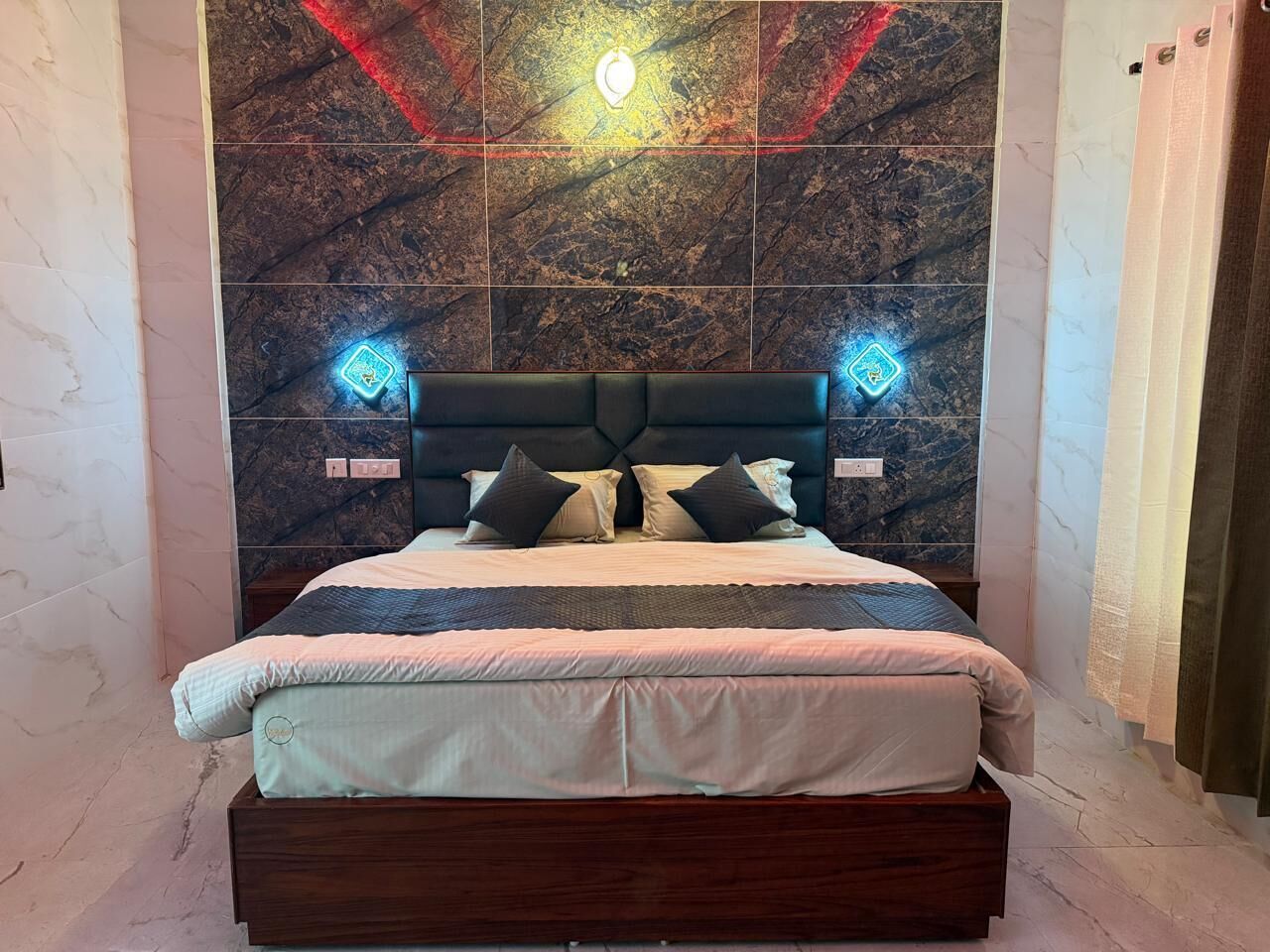 A bed with a dark headboard, two bedside lamps, and a wall with a geometric light fixture.