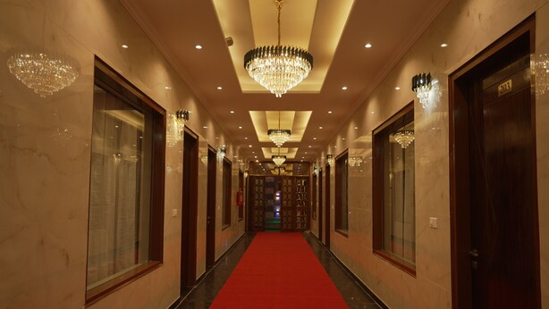 A hotel corridor with a red carpet, chandeliers, and wooden doors. - Hotel Paradise - Chandigarh (Chandigarh)