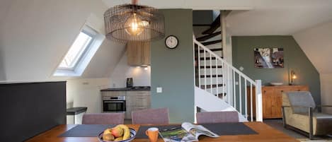 A modern kitchen with a skylight, a dining area with a wooden table, and a staircase leading to another level.